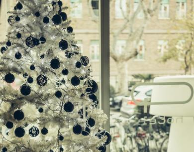 Albero di Natale bianco decorato con palline nere, vicino a una finestra.