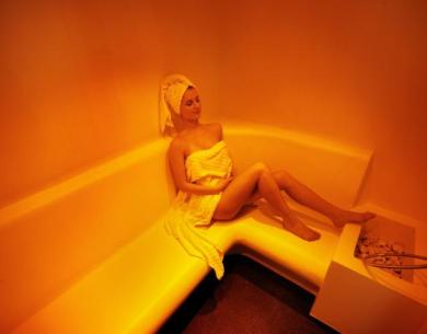Femme détendue dans un sauna avec une serviette blanche.