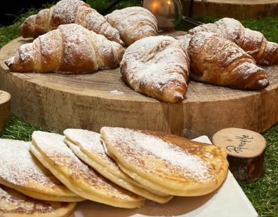 Croissants et pancakes avec du sucre en poudre sur une planche en bois.
