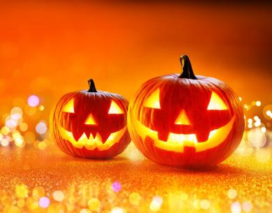 Due zucche di Halloween illuminate su sfondo arancione scintillante.