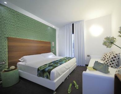 Chambre moderne avec lit double, canapé et décorations vertes.