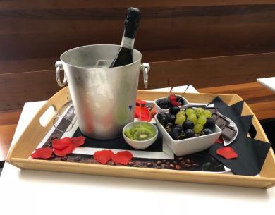 Vassoio con vino, frutta, cioccolato e petali di rosa.
