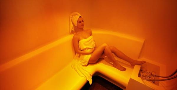 Femme détendue dans un sauna avec une serviette blanche.