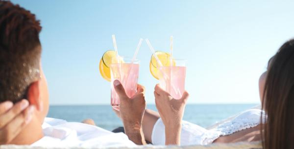 Coppia rilassata sulla spiaggia con cocktail rosa.