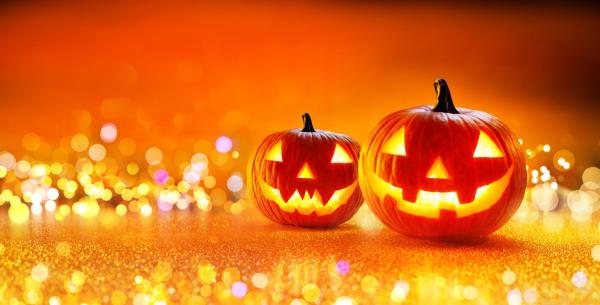 Due zucche di Halloween illuminate su sfondo arancione scintillante.