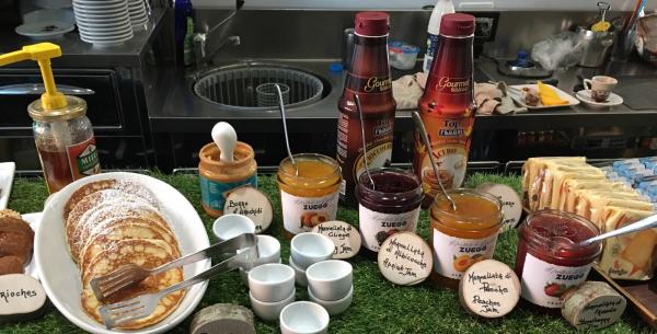 Frühstücksbuffet mit Pfannkuchen, Marmeladen, Erdnussbutter und Sirup.